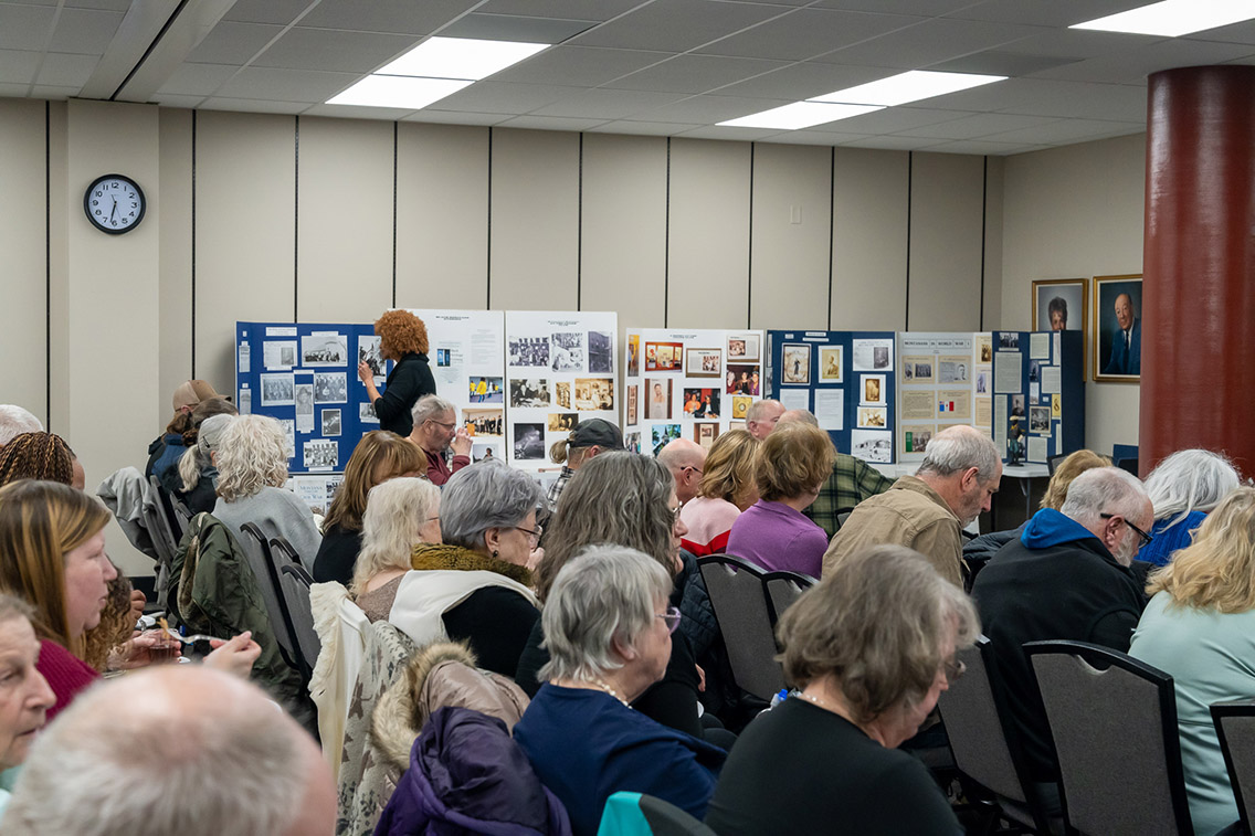 Image of an audience and a display along the side of the wall in a library meeting room